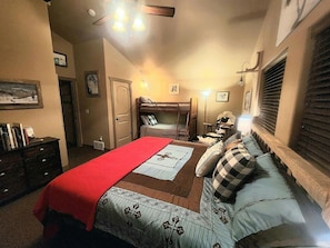 Un dormitorio con una litera, un escritorio, una silla, una lámpara y una cama con una manta roja.