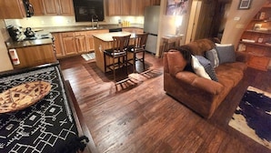 Een keuken met houten kastjes, een eethoek met stoelen, een bank en een vloerkleed.