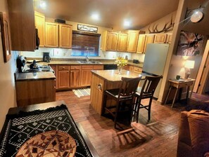 A kitchen with wooden cabinets, a central island, and a dining area with chairs.