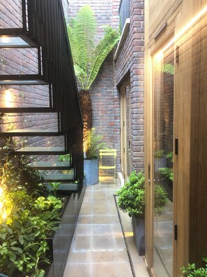 A narrow pathway flanked by potted plants and a brick wall. - Southwark Brick House - Bermondsey London (London)