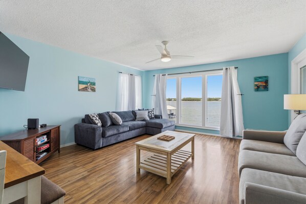 A living room with a sectional sofa, a coffee table, a TV, and a view of the water. - Sea Oats J206 Large 2 bedroom 2 bath Pool,Waterfront,Beach access,Pet friendly (Gulf Shores)