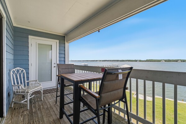 A wooden deck with a table and chairs, overlooking a body of water. - Sea Oats J206 Large 2 bedroom 2 bath Pool,Waterfront,Beach access,Pet friendly (Gulf Shores)