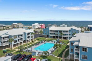 A residential area with a swimming pool surrounded by multi-story buildings, a parking lot, and a view of the ocean. - Sea Oats J206 Large 2 bedroom 2 bath Pool,Waterfront,Beach access,Pet friendly (Gulf Shores)
