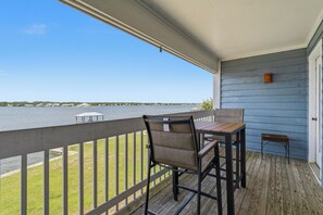 En balkon med et bord og stole, der giver udsigt over vand med bygninger i det fjerne.