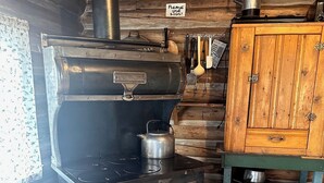 A wood-burning stove with a sign requesting the use of lids, a wooden cabinet, and a metal kettle. - Cabin #3 Cozy one room cabin in charming Gould, perfect for a getaway. (Walden)