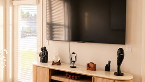 Een moderne woonkamer met een grote flatscreen televisie aan de muur, een houten tv-meubel met een open haard, en een schuifpui naar een terras.