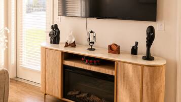 A modern living room with a large flat-screen TV mounted on the wall, a wooden entertainment unit with a fireplace, and a sliding glass door leading to a patio.