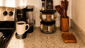 Een keuken met een koffiezetapparaat, een mok, kruidenpotten, houten kommen en keukengerei.