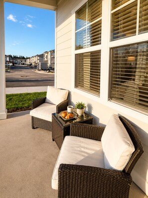 A covered patio with wicker furniture and a small table with a plant and pastries.