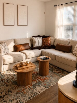 A living room with a beige sofa, two round wooden coffee tables, a chessboard, and a patterned rug.