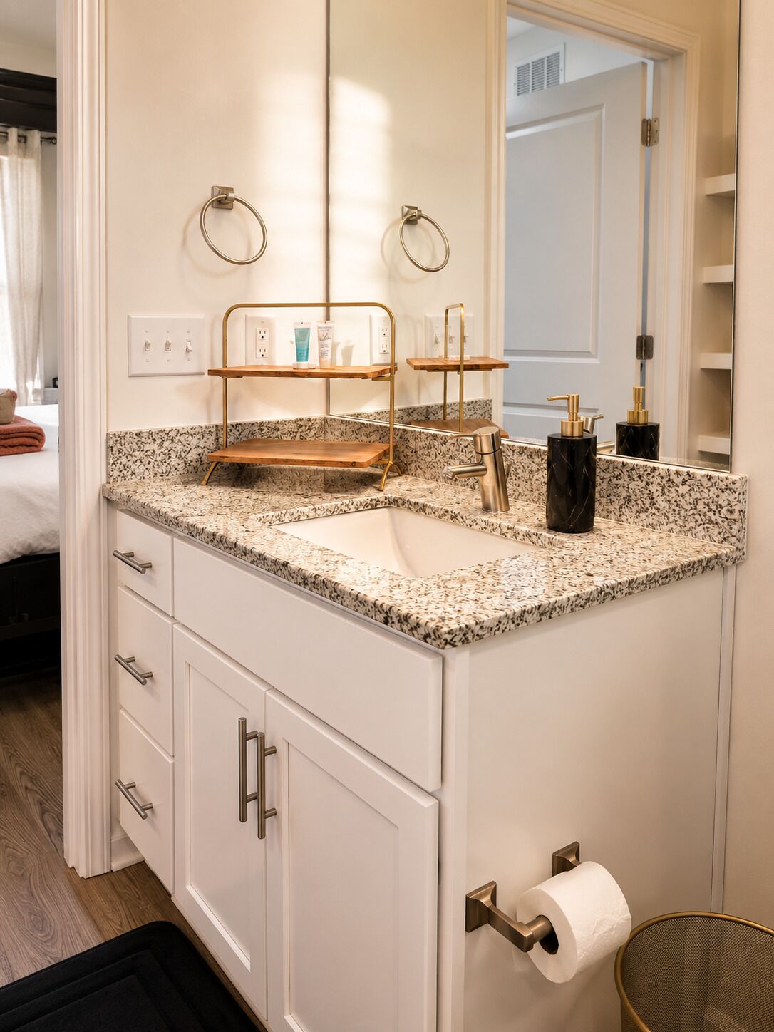 A bathroom with a granite countertop, a double sink, a mirror, a towel rack, and a toilet paper holder.