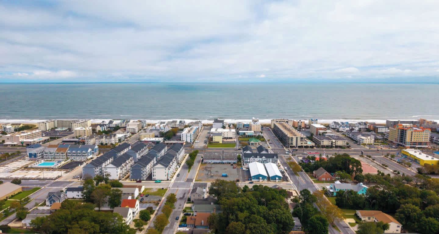 An aerial view of a coastal city with a marina, buildings, and a clear view of the ocean.