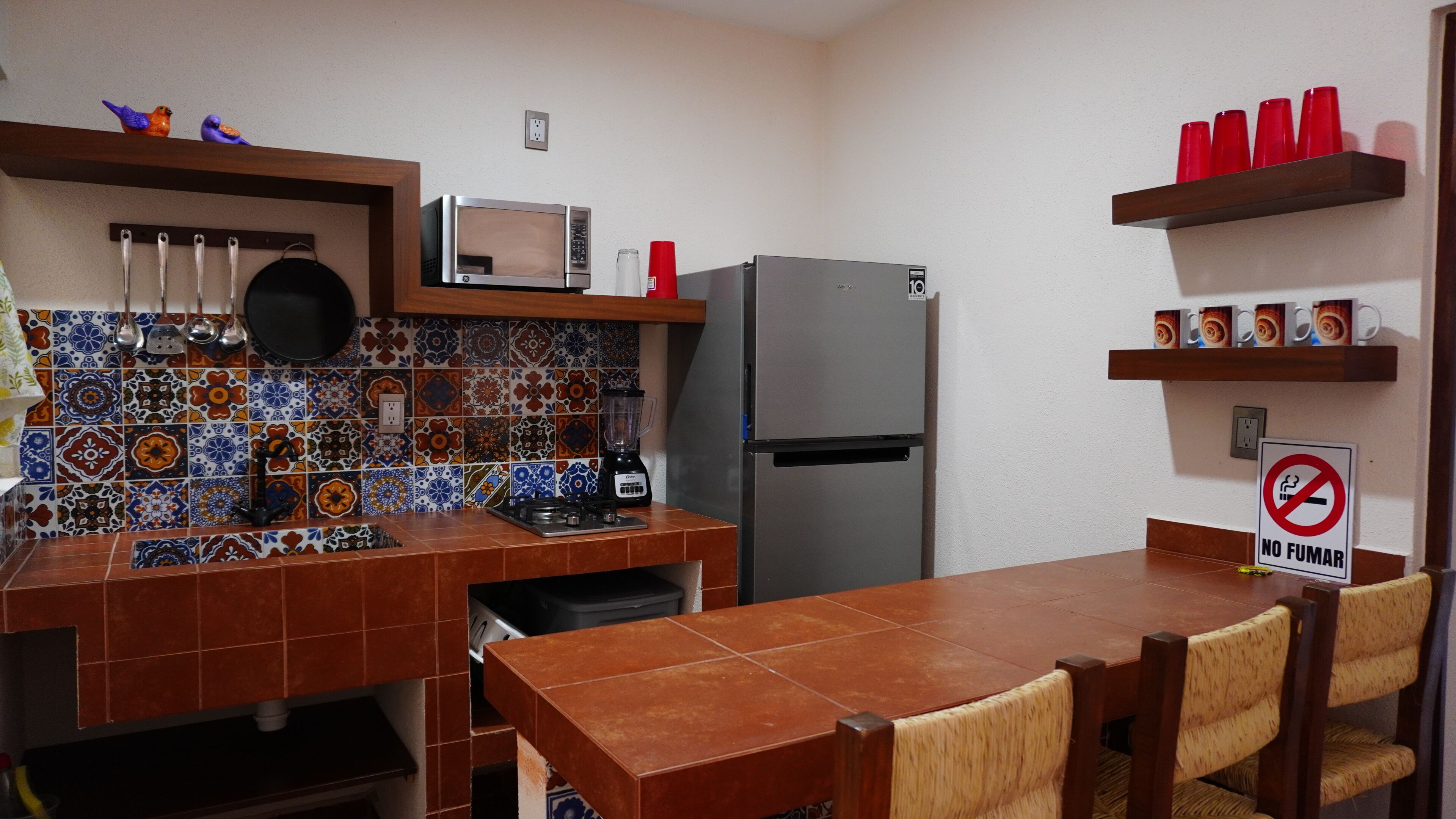 A kitchen with a tiled backsplash, a microwave, a refrigerator, a stove, and a dining table with chairs.