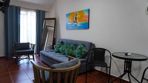 A living room with a sofa, chairs, a painting, and a small table. - Bungalows Huerta del Mar (Santa Cruz)