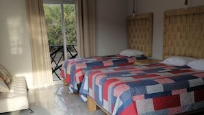 A bedroom with two beds, a sofa, a balcony, and a view of greenery. - Bungalows Huerta del Mar (Santa Cruz)