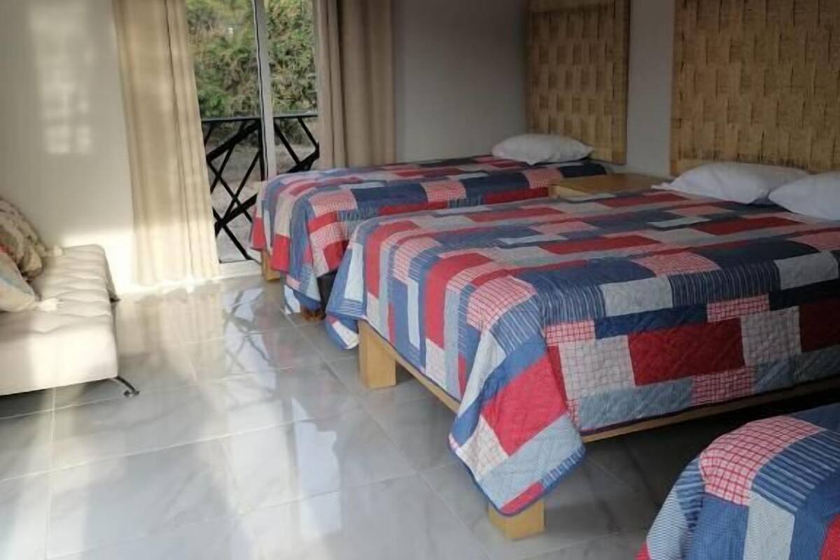 A bedroom with two beds, a sofa, a balcony, and a view of greenery.