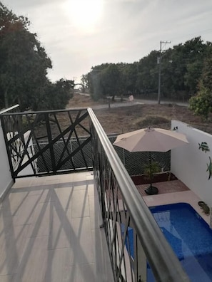 A balcony with a view of trees and a pool area.