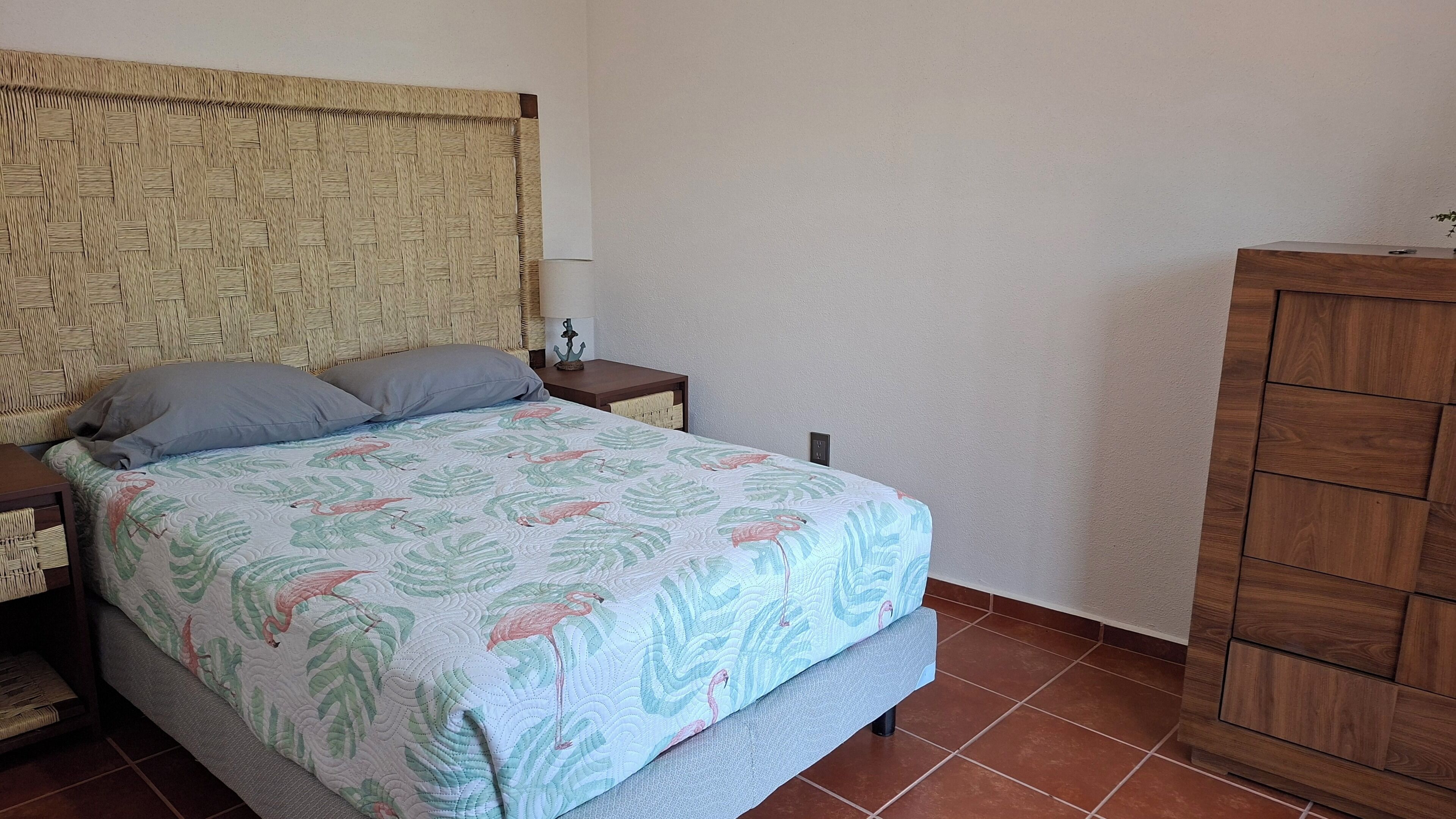 A bedroom with a bed, nightstands, a wooden wardrobe, and a woven headboard.