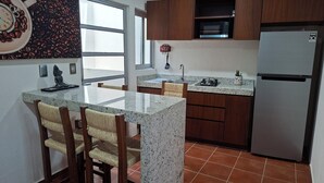 A kitchen with granite countertops, wooden cabinets, a stainless steel refrigerator, and a window. - Bungalows Huerta del Mar (Santa Cruz)