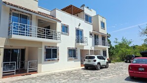 A multi-story building with balconies, a carport, and a cobblestone driveway. - Bungalows Huerta del Mar (Santa Cruz)
