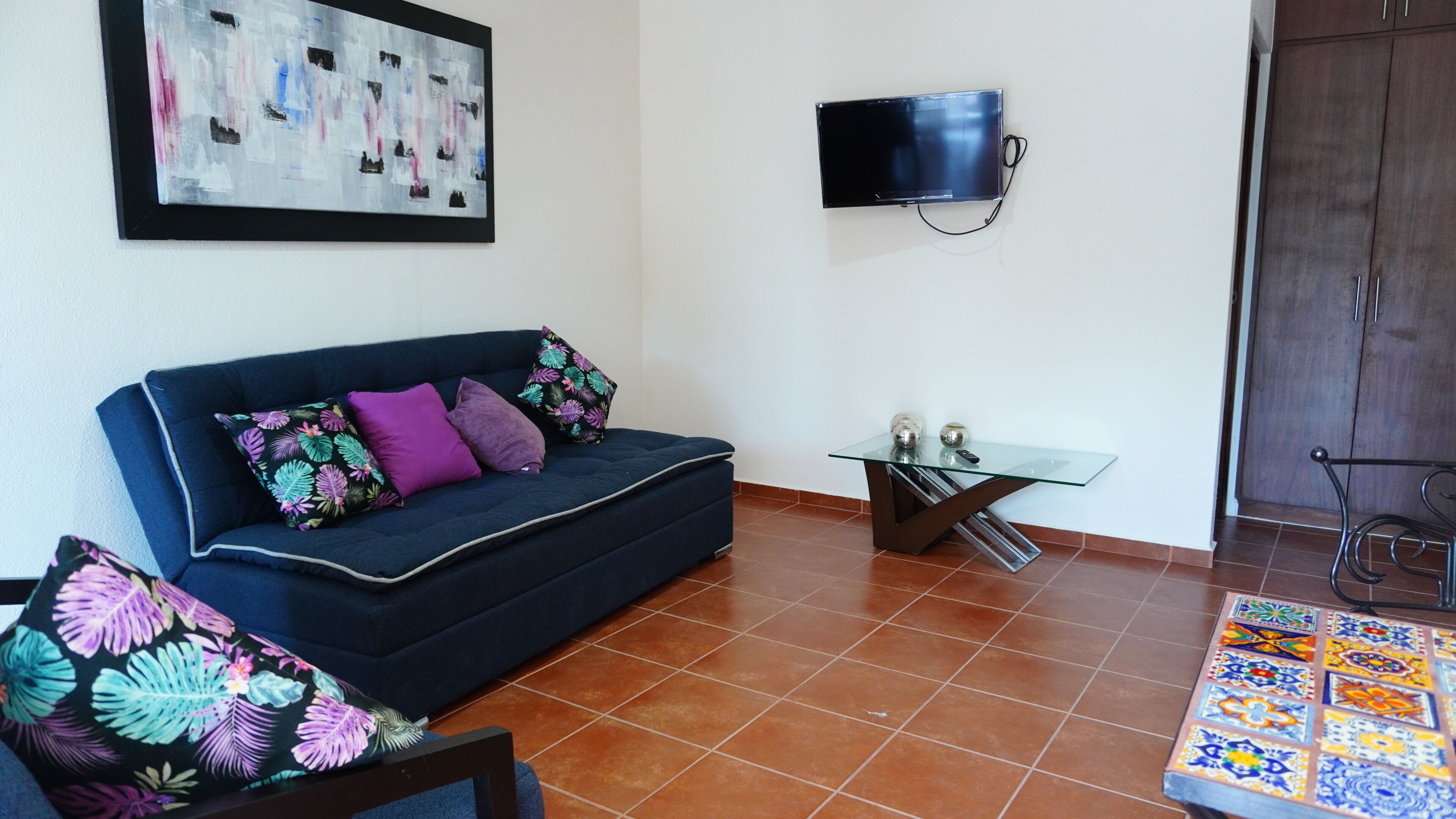 A living room with a sofa, a glass coffee table, a television, and a tiled floor.
