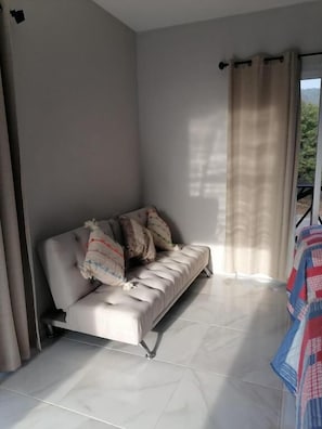 A modern room with a sofa, curtains, and a view of greenery outside.