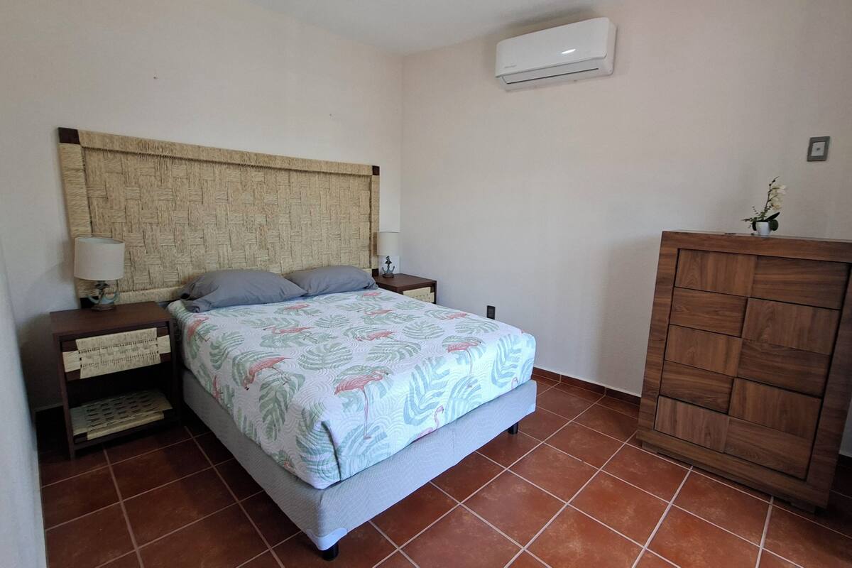 A bedroom with a bed, nightstands, a wooden wardrobe, and an air conditioning unit.