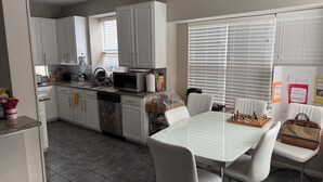 Une cuisine avec des meubles blancs, un four à micro-ondes, un évier et un coin repas comprenant une table et des chaises.