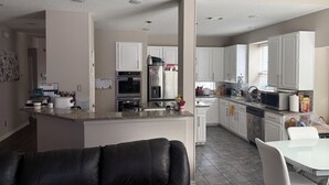 Une cuisine moderne avec des meubles blancs, un îlot central et un coin repas comprenant une table et des chaises blanches.