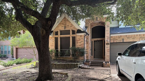 Une maison d’habitation avec une façade en briques, un garage et une allée où est garée une voiture.