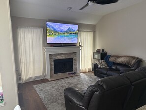 Ein Wohnzimmer mit Kamin, einem flachbildfernseher darüber, einem Ledersofa und einem Deckenventilator.