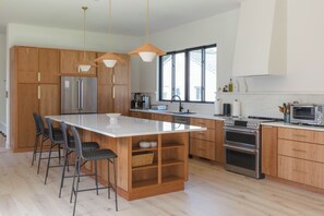 Eine moderne Küche mit Holzschränken, Edelstahlgeräten und einer großen Kochinsel mit Barhocker.