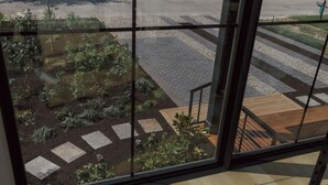 Blick durch ein Fenster auf einen Gartenbereich mit trittsteinförmigen Wegen, einer Holzdielen-Terrasse und einer Metalltreppe.