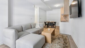 A modern living room with a grey sectional sofa, a wooden coffee table, a fluffy rug, a dining area with a table and chairs, and a built-in TV. - Home Richmond Hill 2bed2bath | Parking (Richmond Hill)