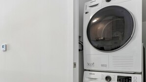A stacked washer and dryer unit in a room with a plain white wall and wooden flooring. - Home Richmond Hill 2bed2bath | Parking (Richmond Hill)