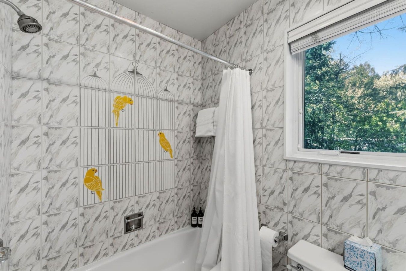 Un baño con bañera, ducha y ventana con vistas a árboles.