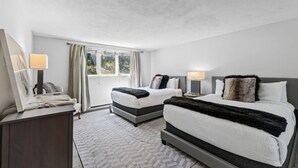 Ein Hotelzimmer mit zwei Betten, einem großen Fenster, einem Schreibtisch mit Lampe und einem Spiegel.
