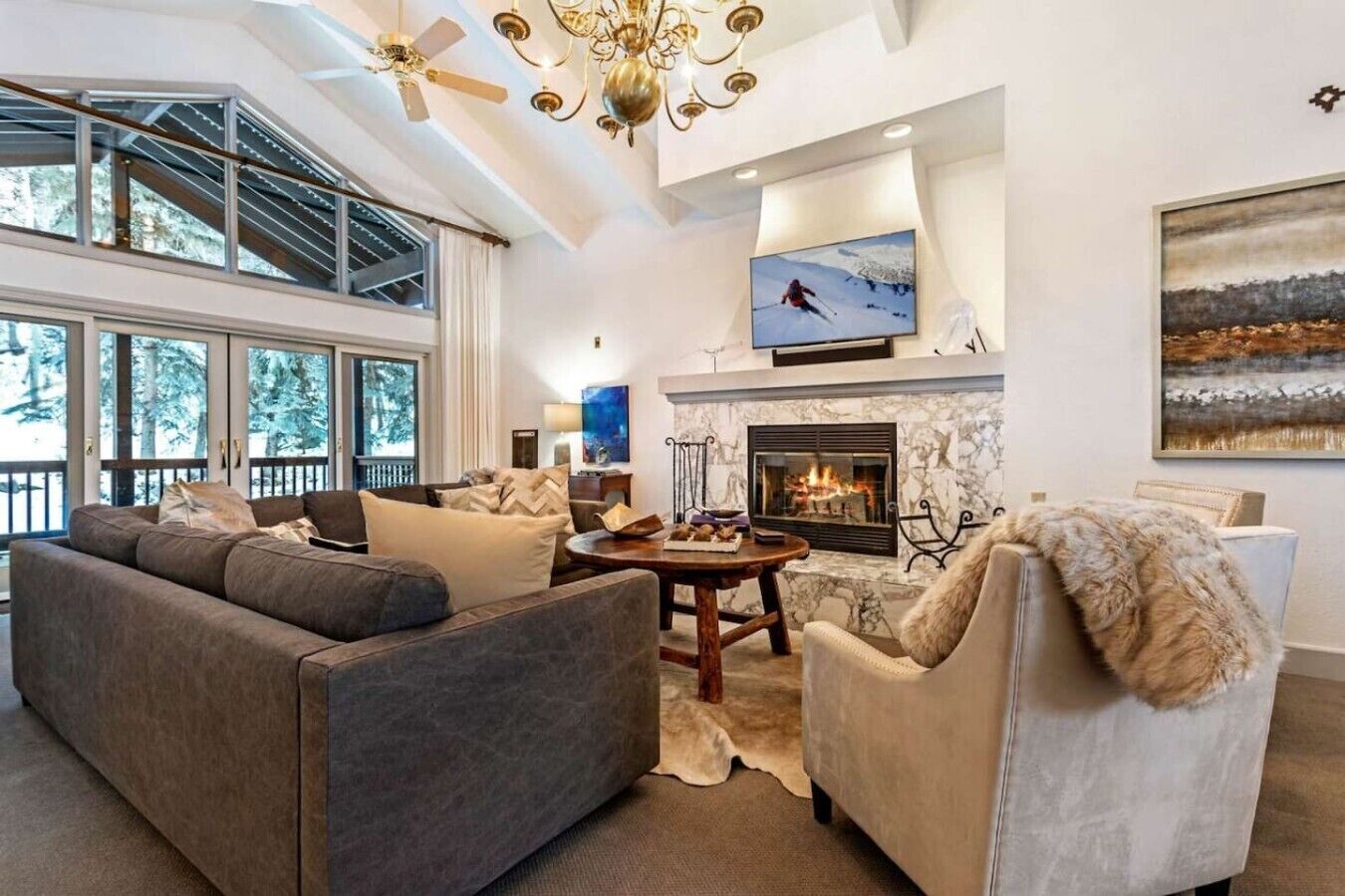 A modern living room with a fireplace, large windows, and a ceiling fan.
