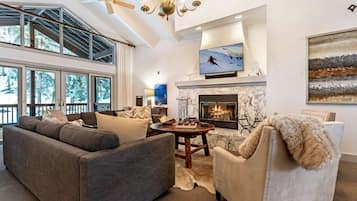 A modern living room with a fireplace, large windows, and a ceiling fan.