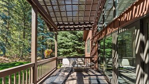 Eine überdachte Terrasse im Freien mit Tisch und Stühlen, umgeben von Glaswänden und einem Holzgeländer.