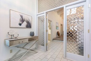 A hallway with a white tiled floor, a wooden console table with decorative items, a framed painting, and a glass door with a metal grid. - Family Friendly Eagle Vail Retreat W/Hot Tub (Avon)