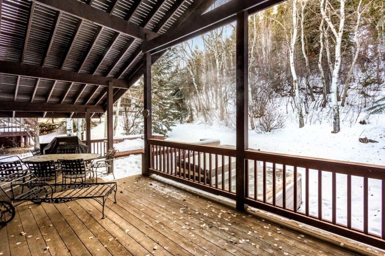 Un espacio al aire libre cubierto con una terraza de madera, sillas de metal y una mesa.