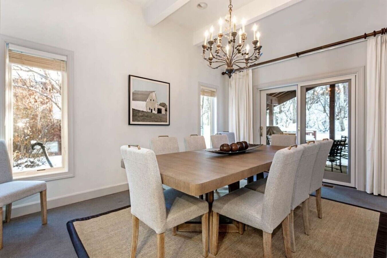 A dining room with a large table, chairs, a chandelier, and a picture on the wall.