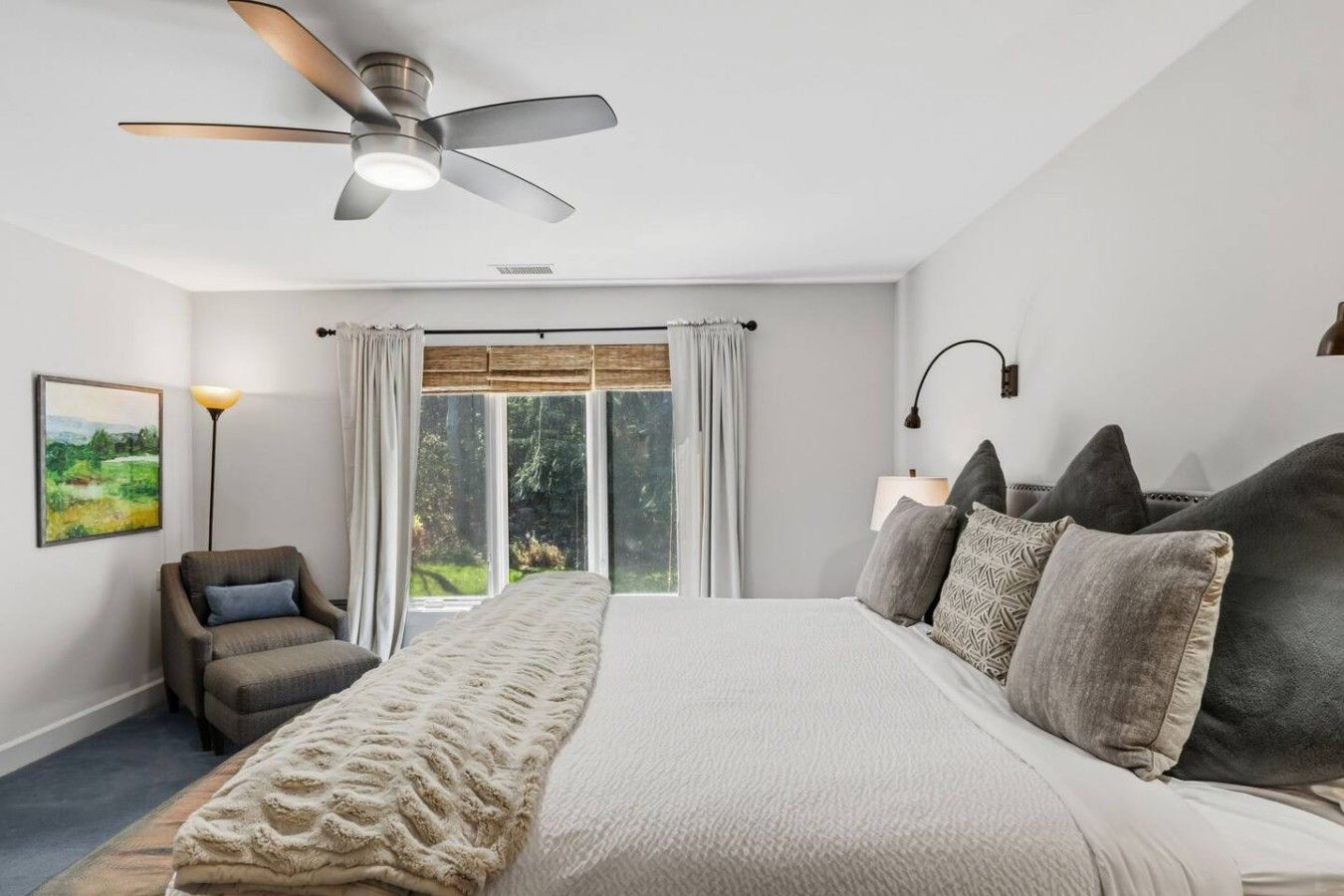 Ein Schlafzimmer mit einem Bett, einem Sessel, einer Stehlampe, einem Deckenventilator und einem Fenster mit Vorhängen.