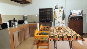 Eine Küche mit Esstisch, Stühlen, einem Kühlschrank, einem Herd und einem Fernseher.