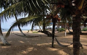 A beach with palm trees, a hammock, and a building in the background.
