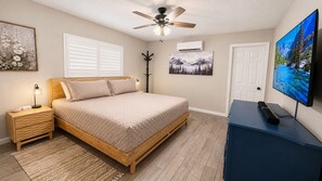A bedroom with a bed, bedside table, lamp, ceiling fan, artwork, air conditioning unit, door, and a television on a dresser. -  Monte Mariposa Casita:Near Yosemite,3 Private Acres,King Suite,2 Fire Pits (Mariposa)