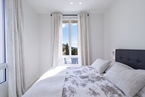 Ein Schlafzimmer mit einem großen Bett, Blick durch ein Fenster und einem Balkon.