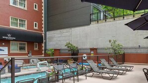 Een buitenzwembad met ligbedden en parasols, een gebouw met een 'WORLDMARK BY WYNDHAM'-bordje en een betonnen muur.