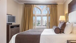 Een hotelkamer met een bed, een bureau met een computer, een telefoon en een raam met gordijnen.